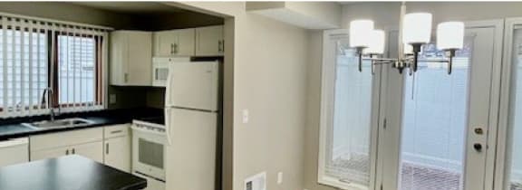 Apartment kitchen with white cabinetry, appliances, kitchen breakfast bar, dining area and access to private patio