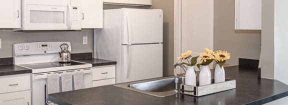 View of apartment kitchen with white appliances & cabinetry as well as a breakfast bar and pantry