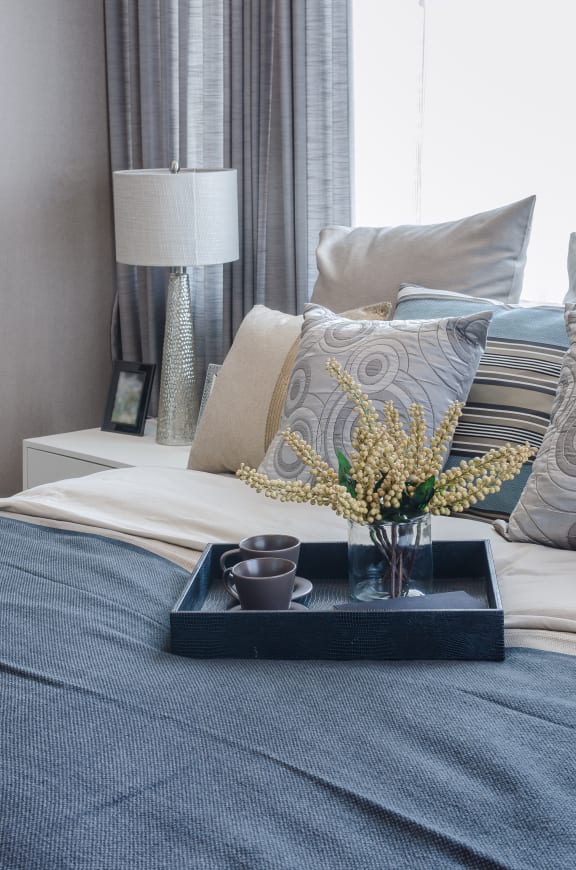 a tray with flowers on a bed with pillows and a lamp