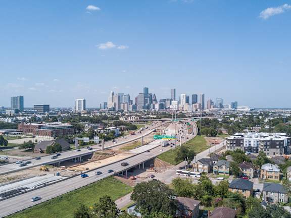 A cityscape with a clear blue sky and a highway in the foreground.