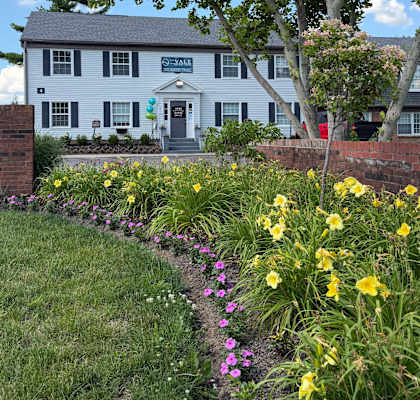 A white building with a grey roof and a garden in front.