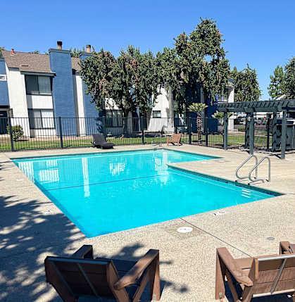 A swimming pool surrounded by chairs and trees.