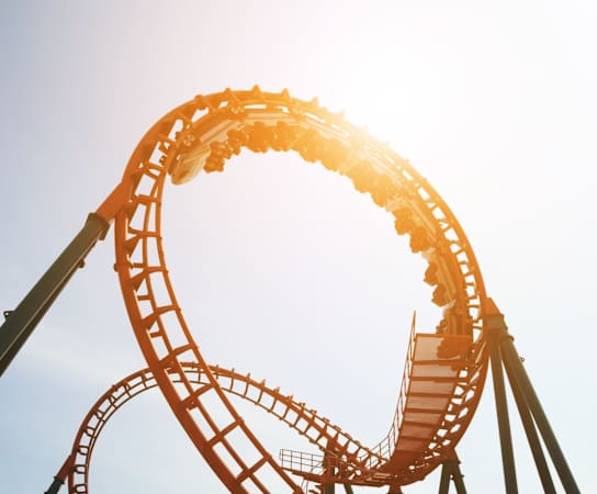 A roller coaster track curves upwards against a clear sky.