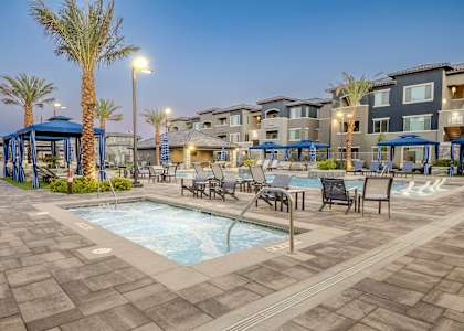 A pool area with a hot tub and lounge chairs in front of apartment buildings.