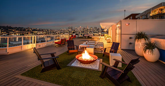 A rooftop patio with a fire pit and chairs overlooking a city skyline at dusk. at The Summit at Lake Union, Seattle, WA, 98109