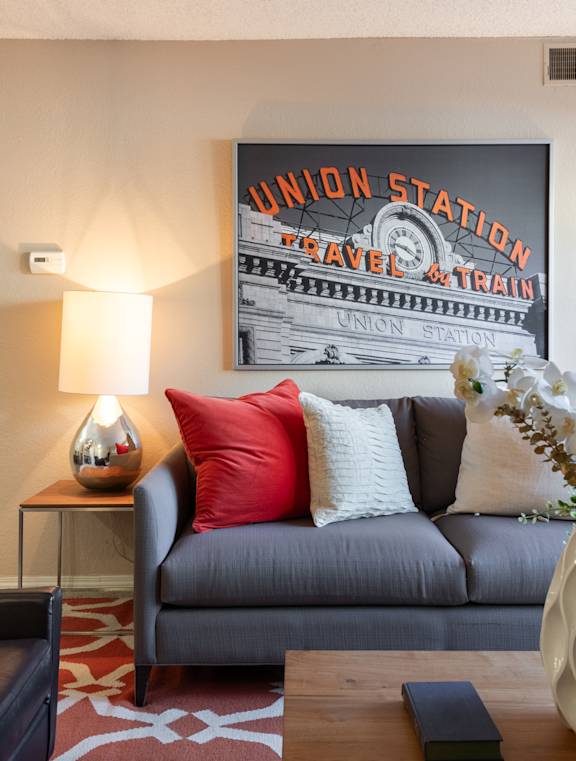 A grey couch with a lamp and a picture of a train on the wall.