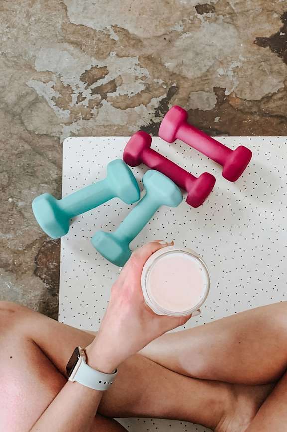 A person is holding a glass of milk and lifting two dumbbells.