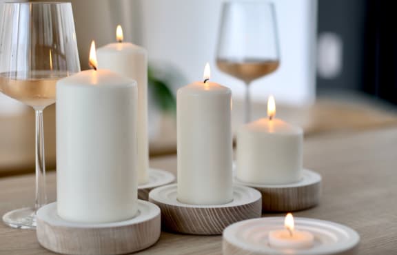 White lit candles and wine glass with white wine in them on a wooden table. 