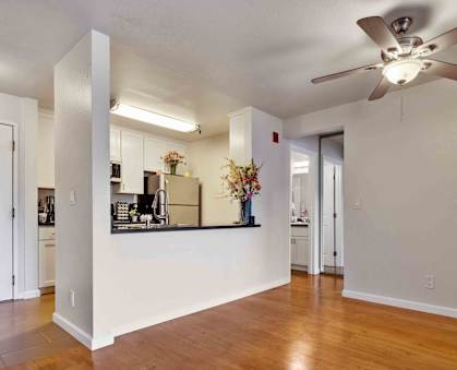 an empty living room with a ceiling fan and a kitchen