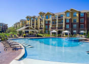 Thumbnail 2 of 42 - a large swimming pool with lounge chairs and umbrellas in front of an apartment building  at WaterCrest at City Center, Lenexa, KS, 66219