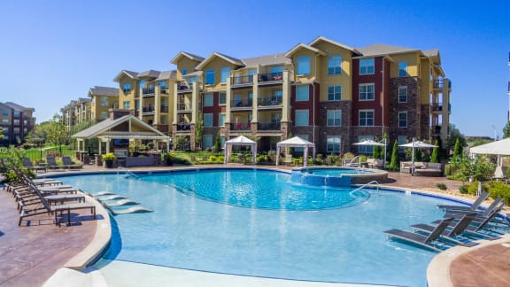 a large swimming pool with lounge chairs and umbrellas in front of an apartment building  at WaterCrest at City Center, Lenexa, KS, 66219