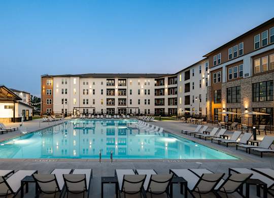 A large swimming pool surrounded by lounge chairs in front of a hotel.