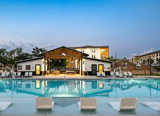 A large swimming pool in front of a building with lounge chairs around it.