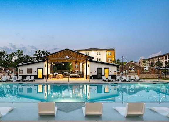 A large swimming pool in front of a building with lounge chairs around it.