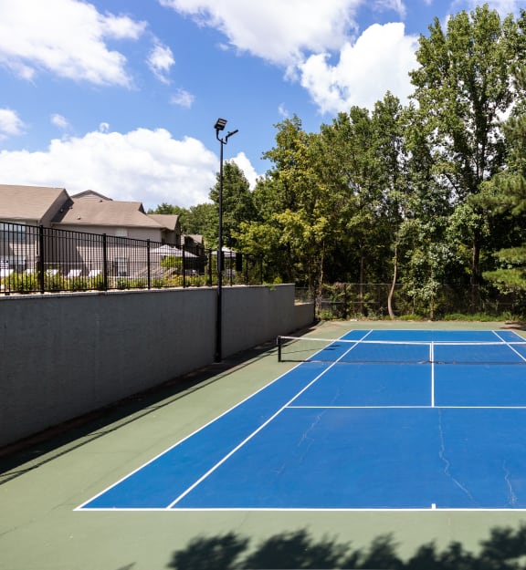 a blue tennis court with a fence and trees
