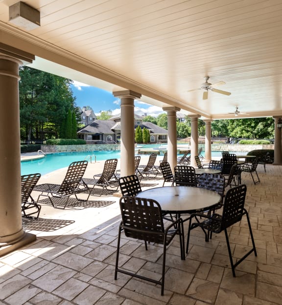 a covered patio with tables and chairs next to a swimming pool