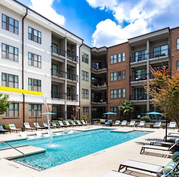 a swimming pool with lounge chairs in front of an apartment building