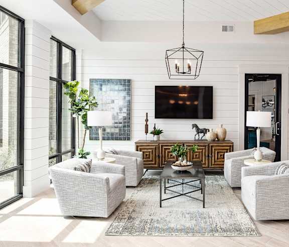 A modern living room with a white sofa set, a coffee table, and a large flat-screen TV mounted on the wall.