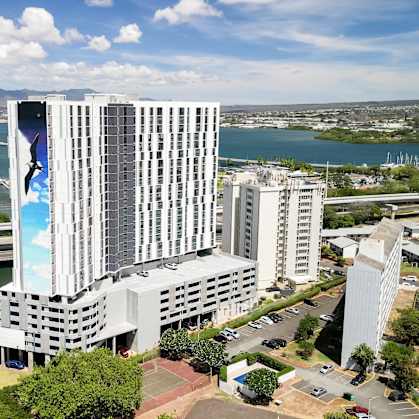 A large white building with a blue mural on the side is situated next to a river.