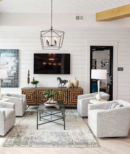 A modern living room with a white sofa set, a coffee table, and a large flat-screen TV mounted on the wall.