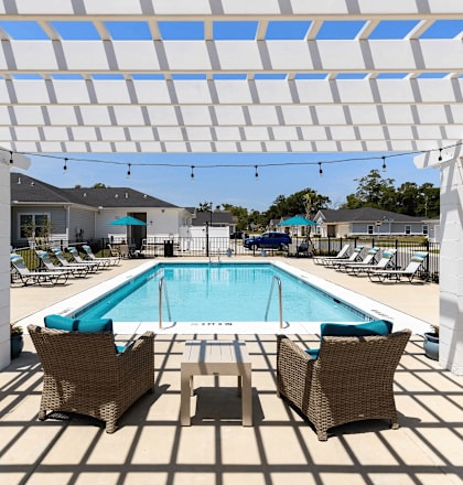 A pool area with a white pergola and chairs.
