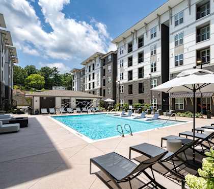 A pool area with sun loungers and umbrellas in front of a building.
