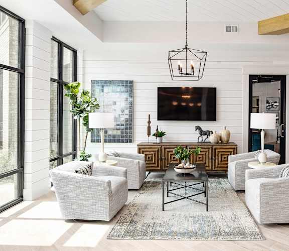 A modern living room with a white sofa set, a coffee table, and a large flat-screen TV mounted on the wall.