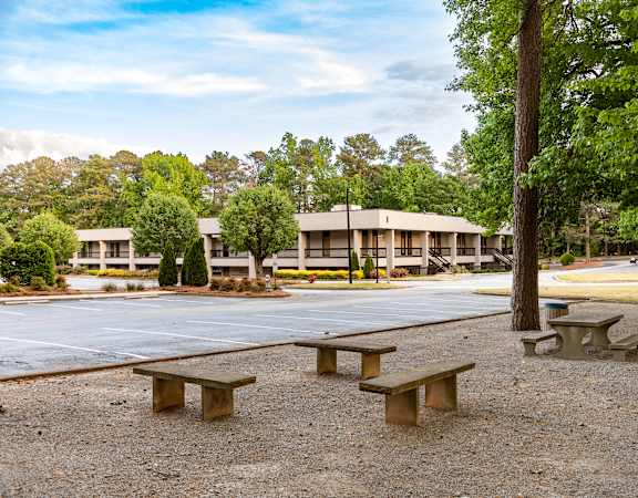 A park with picnic tables and benches in front of a building.