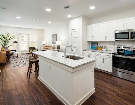 an open kitchen and living room with white cabinets and a counter top