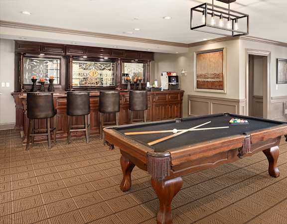 A pool table is in the middle of a room with a bar and chairs.