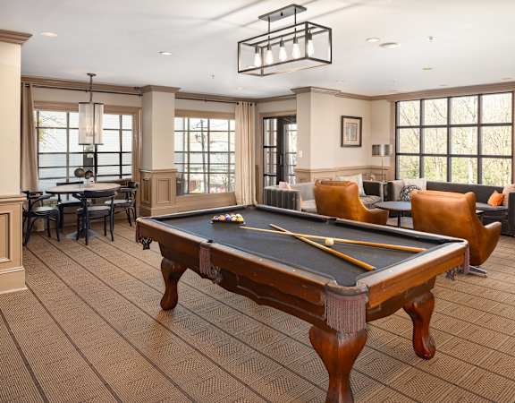 A pool table is in the middle of a room with a brown floor and a large window.