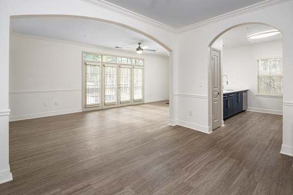 an empty living room and kitchen with wood flooring and white walls