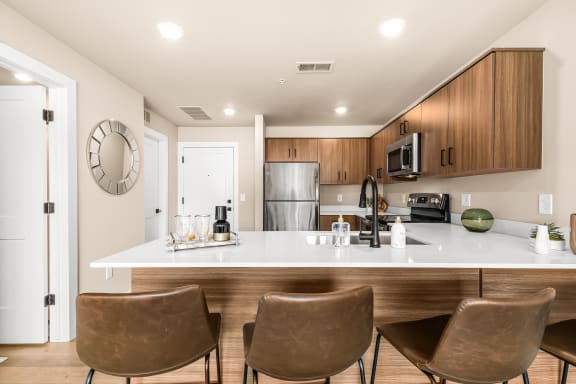 a kitchen with white countertops and a large white island with four brown chairs in front of
