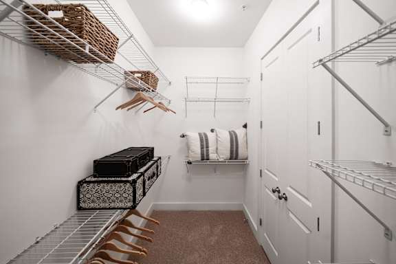 a walk in closet with white walls and white closets and shelves and a closet