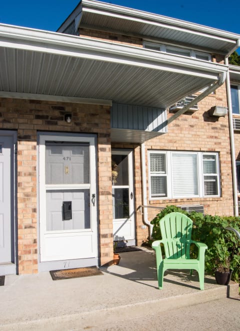 a green chair in front of a brick house with a white door at Brookwood at Oakdale 55+, New York