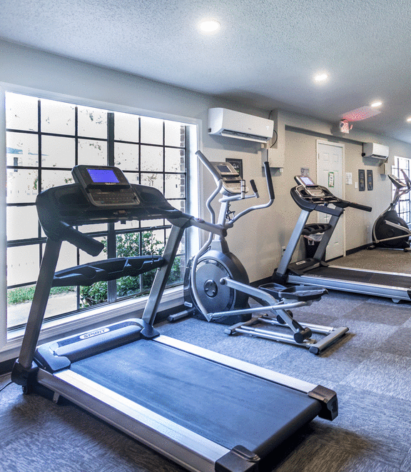 two treadmills and other exercise equipment in a gym with a window at Azure Place Apartments, Memphis, Tennessee
