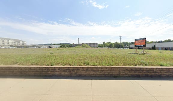 A billboard in the middle of a grassy field with a building in the background.