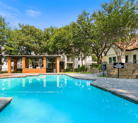 A swimming pool surrounded by trees and a building in the background.