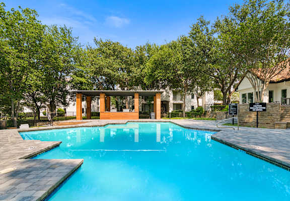 A swimming pool surrounded by trees and a building in the background.
