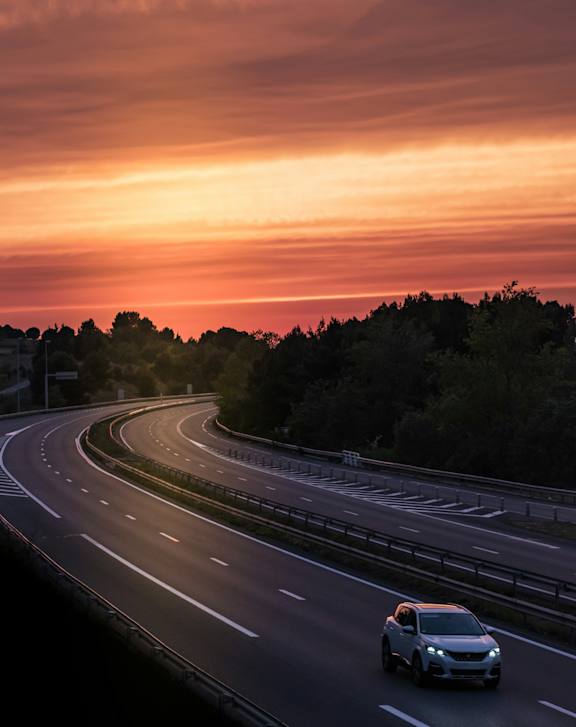 A car is driving on a highway during sunset.