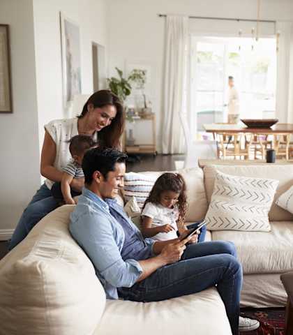 a family sitting on a couch in a living room looking at a tablet