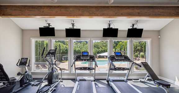 A gym with treadmills, exercise bikes, and a ceiling fan.