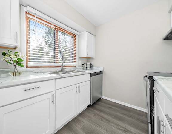 A kitchen with white cabinets and a window with blinds.