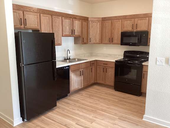 A black refrigerator is in a kitchen with wooden cabinets.