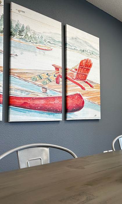 A wooden table with a bowl of bread and a painting of a red canoe on the wall.
