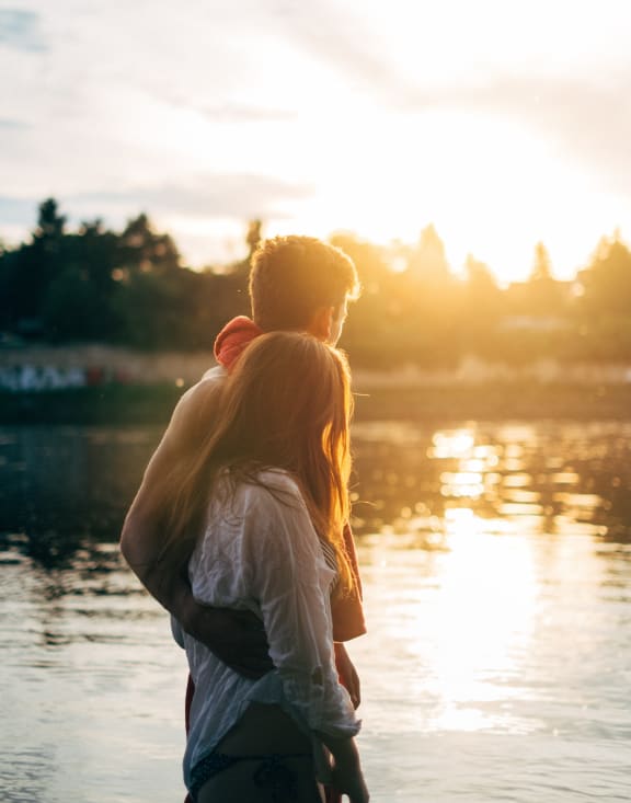 a mother and child look out over a lake at sunset
