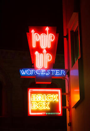 A neon sign for a place called "Brick Box" is lit up at night.