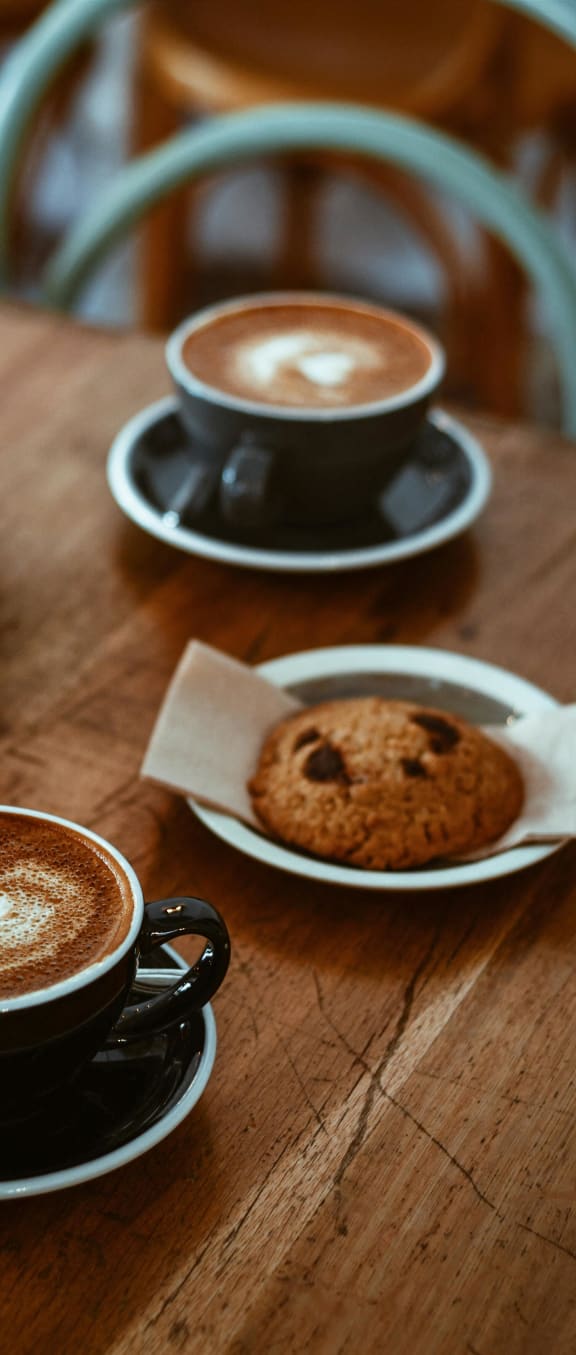 two cups of coffee and a cookie on a wooden table
