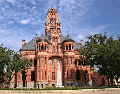 A large red building with a clock tower and a statue in front.