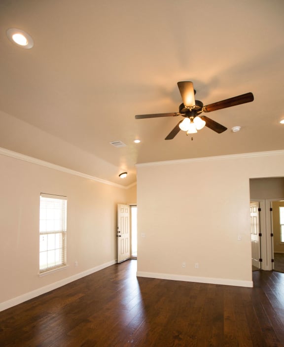 an empty living room with a ceiling fan and a kitchen